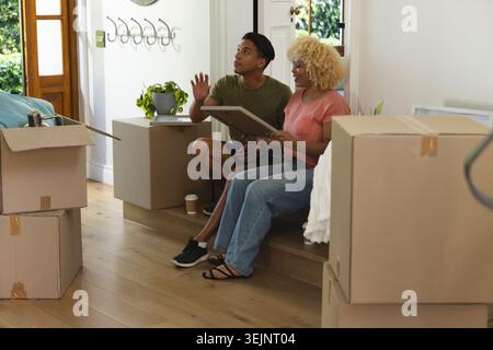 Verschiedene Pärchen sitzen auf dem Eingang und halten ein gerahmtes Bild und besprechen, wo man in der Nähe von Kisten hängen sollte. Pappe, Auspacken, Spiegel, Stockfoto
