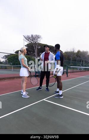Verschiedene Coaching-Gruppen, die den Gesten des Trainers auf dem Hartplatz lauschen und dabei Tennisausrüstung mit Schlägern tragen. Training, Outdoor, Athlet Stockfoto