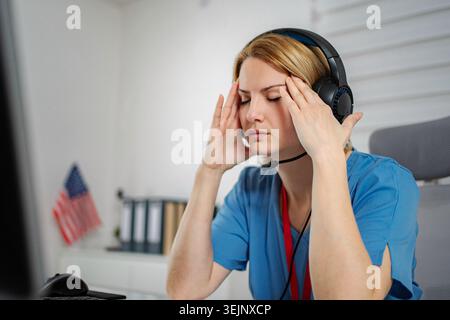 Gestresste Frau im Headset mit Migräne am Arbeitsplatz Stockfoto