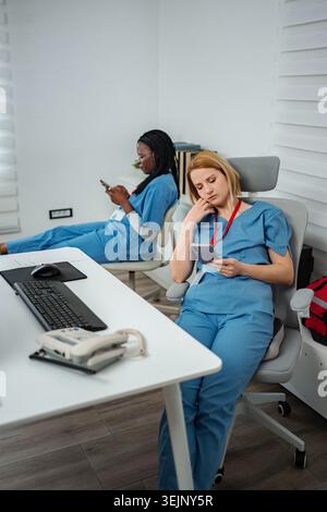 Überlastete Krankenschwestern erleben Burnout, ruhen sich aus, benutzen Mobiltelefone Stockfoto