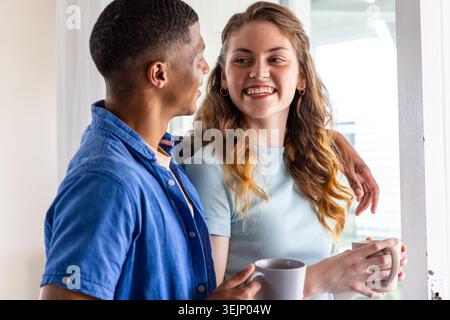 Verschiedene Paare stehen an der Tür und halten Keramikbecher, Mann hängt Arm um Frau. Lifestyle, offen, gemütlich, sonnig, intim Stockfoto