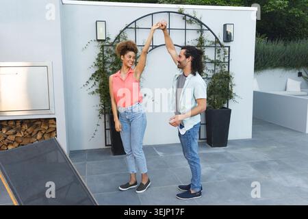 Verschiedene Paare tanzen auf der gefliesten Terrasse zu Hause in der Nähe von Gitter und eingebautem Grill und tragen legere Schuhe. Im Freien, Terrasse, Minimalis Stockfoto