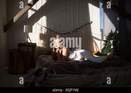 Die junge Frau liegt an den Weihnachtsferien am sonnigen Tag auf dem Bett. Hygge-Konzept. Stockfoto