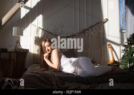Die junge Frau liegt an den Weihnachtsferien am sonnigen Tag auf dem Bett. Hygge-Konzept. Stockfoto