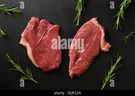 Rohes marmoriertes Ribeye-Steak mit Rosmarinzweig auf schwarzem Hintergrund. Stockfoto