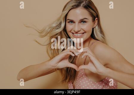 Blonde Frau macht mit ihren Händen Herzform Stockfoto