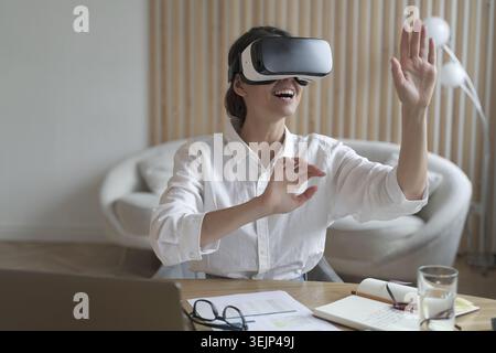 Glückliche Büroangestellte mit vr-Brille, die bei der Arbeit mit der virtuellen Realität interagiert Stockfoto