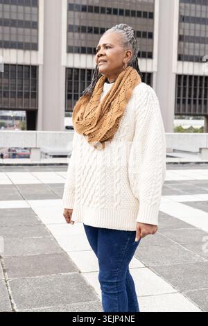 Ältere Afroamerikanerin, die auf dem Dach steht und einen Zopfstrick-Pullover mit Infinity-Schal trägt Stockfoto