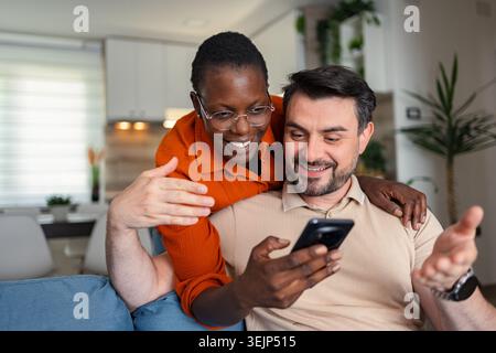 Glückliches Paar, das zu Hause ein Smartphone nutzt, lustige Videos ansieht und Spaß hat Stockfoto