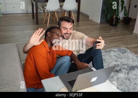 Glückliche Paare, die Familie und Freunde über Laptop und Smartphone zu Hause anrufen Stockfoto