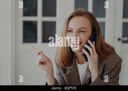 Geschäftsfrau ruft an und lächelt. Elegante, glückliche Frau im mittleren Erwachsenenalter arbeitet von zu Hause aus. Stockfoto