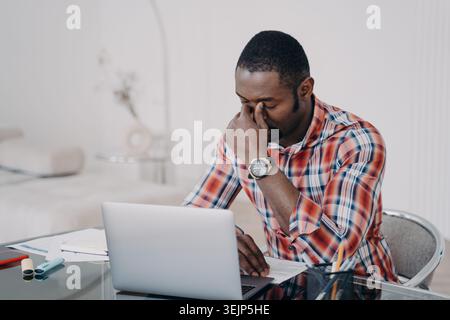 Konzentrierter, müder afroamerikanischer Geschäftsmann löst Geschäftsprobleme bei der Arbeit am Laptop. Stress am Arbeitsplatz Stockfoto