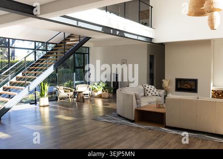 Beigefarbene Sofas, die sich um einen niedrigen Couchtisch in einem offenen Wohnbereich gruppieren, Glaswand, die den Garten freigibt Stockfoto