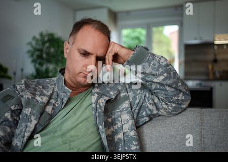 Depressiver Soldat, der zu Hause auf dem Sofa sitzt und an posttraumatischer Belastungsstörung leidet Stockfoto