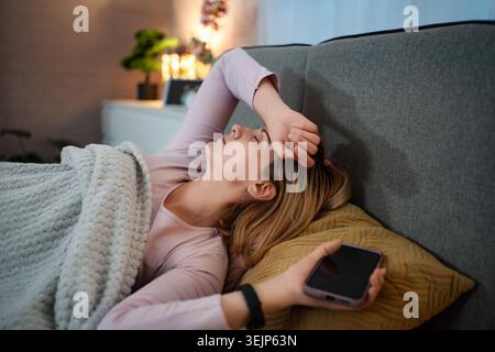 Frau, die im Bett liegt und sich unwohl und erschöpft fühlt Stockfoto