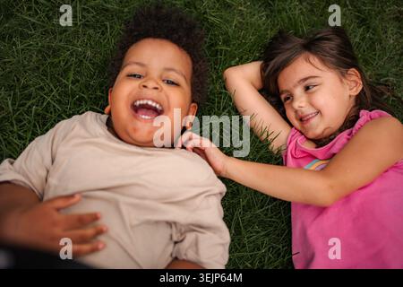 Kinder lachen und spielen zusammen auf Gras liegen Stockfoto