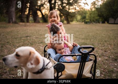 Glückliche Kinder, die im Wagen mit Hund im Park spielen Stockfoto