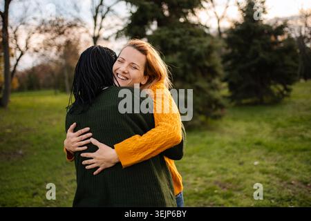 Glückliche junge Freundinnen, die sich im Park umarmen Stockfoto