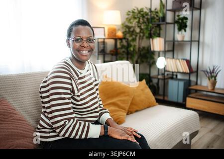 Glückliche junge Erwachsene Frau, die sich zu Hause auf dem Sofa entspannt Stockfoto