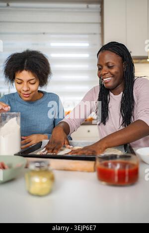 Glückliche afroamerikanische Mutter und Tochter, die zusammen Pizza machen Stockfoto