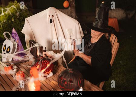 Ältere Frau trägt Hexenkostüm, die Halloween mit Geisterkostüm in der Nacht feiert Stockfoto