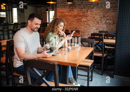 Junges Paar, das Smartphones benutzt, während er in einem Restaurant Kaffee trinkt Stockfoto