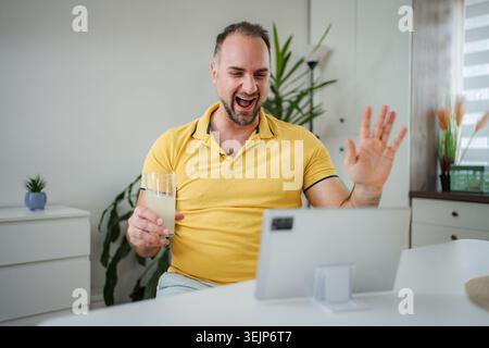 Glücklicher Mann, der Videoanruf hat, der mit einem Drink winkt Stockfoto