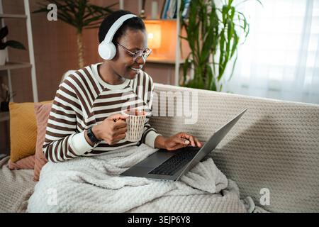 Junge Erwachsene Frau, die sich mit Laptop auf dem Sofa entspannt Stockfoto