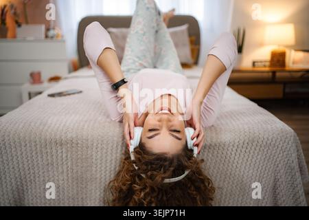 Junge Frau, die Musik genießt und sich zu Hause auf dem Bett entspannt Stockfoto
