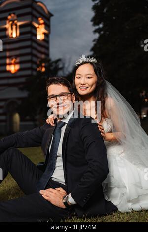 Interrassisches Brautpaar lächelt, während er auf Gras sitzt Stockfoto