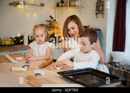 Glückliche Familienmutter und zwei Kinder machen Weihnachtskekse und haben Spaß zu Hause in der Küche. Kinder Geschwister machen ho Stockfoto
