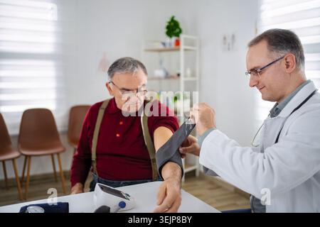 Der behandelnde Arzt überprüft den Blutdruck eines Seniorpatienten in der Klinik Stockfoto