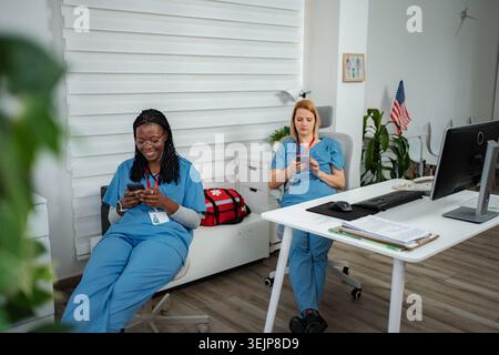 Zwei Krankenschwestern überprüfen Smartphones in der Pause in der Arztpraxis Stockfoto
