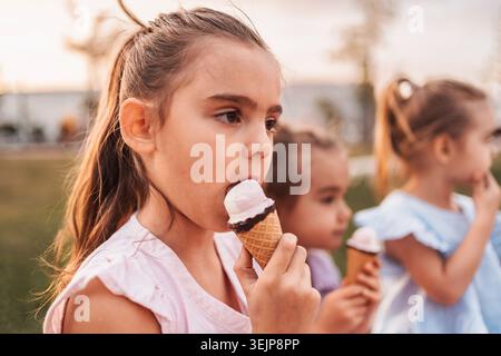 Kinder genießen Eiskegel in einem Park bei Sonnenuntergang Stockfoto