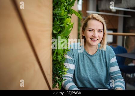 Blonde Frau lächelt in einem modernen Café mit grüner Wand Stockfoto