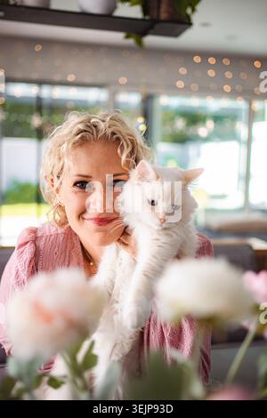 Frau lächelt und hält ihre flauschige weiße Katze Stockfoto