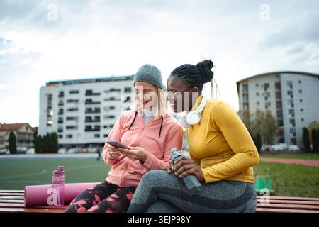 Verschiedene Freundinnen, die sich nach dem Training mit dem Smartphone ausruhen Stockfoto