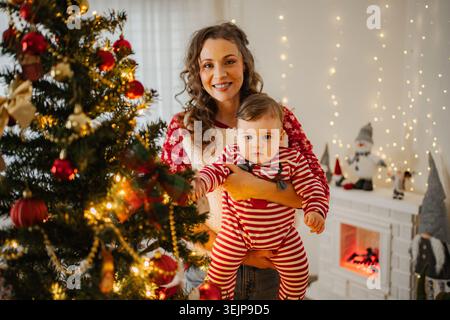 Mutter hält den kleinen Sohn fest, der zu Hause Weihnachtsfeiertage feiert Stockfoto