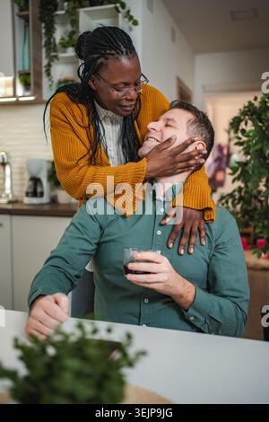 Liebevolles interrassisches Paar, das sich in moderner Küche zu Hause umschließt Stockfoto