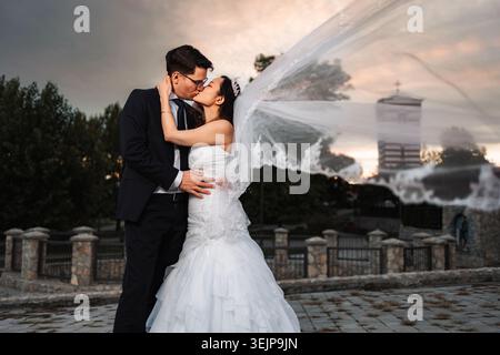 Interrassisches Brautpaar, das sich unter dramatischem Himmel küsst Stockfoto