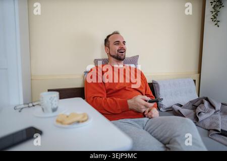 Glücklicher Erwachsener, der sich im Bett entspannt und Fernsehen guckt Stockfoto