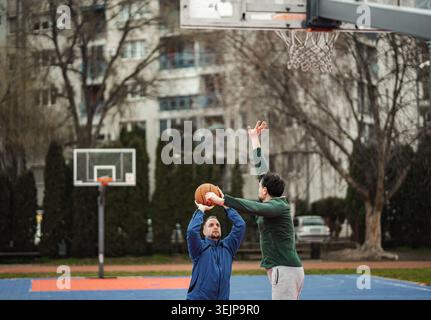 Zwei Männer spielen draußen Basketball und blockieren Schuss Stockfoto