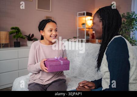Die Tochter schenkt der glücklichen Mutter zu Hause ein Geschenk Stockfoto