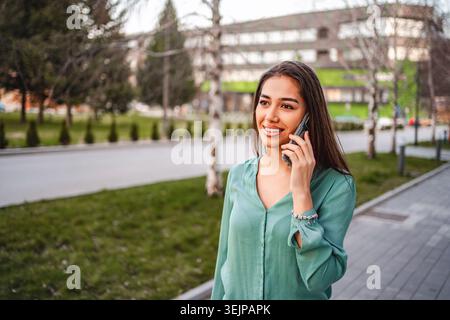 Eine junge Frau lächelt, während sie im Park telefoniert Stockfoto