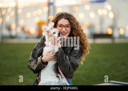 Junge Frau, die einen kleinen Hund im Park bei Sonnenuntergang umschließt Stockfoto