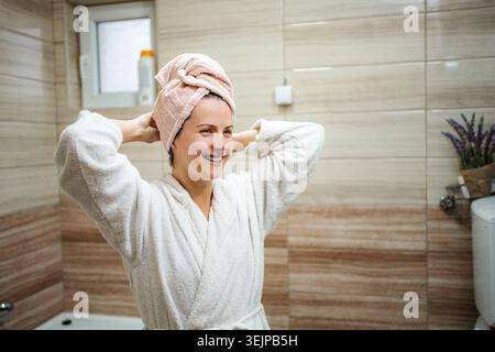 Junge Frau lächelt im Bademantel mit handtuchumwickelten Haaren Stockfoto