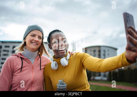 Verschiedene Freundinnen lächeln und machen nach dem Training Selfie im Freien Stockfoto