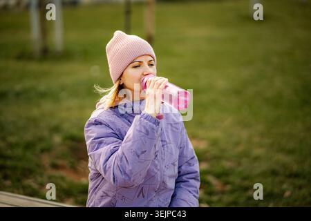 Frau trinkt Wasser aus wiederverwendbarer Flasche im Freien nach dem Training Stockfoto