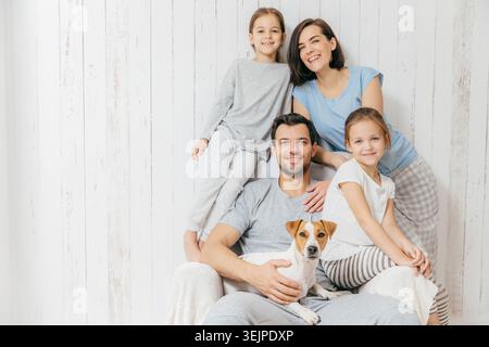 Porträt der glücklichen Familie drinnen. Ein hübscher Vater hält Hund, eine schöne brünette Mutter und zwei Töchter, haben Spaß miteinander, posieren Stockfoto