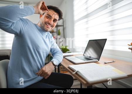 Porträt eines lächelnden Mannes am Schreibtisch und Laptop Stockfoto